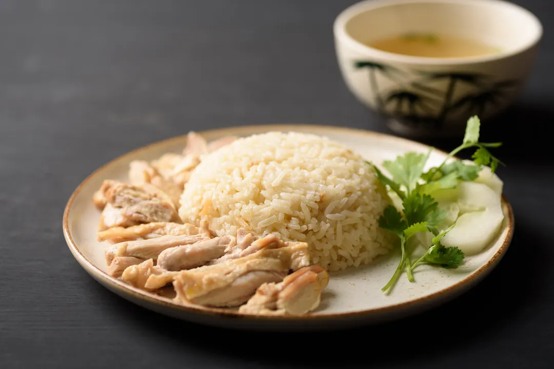 Hainanese chicken rice with coriander, cucumber and chicken soup on black background. Local food in East and Southeast Asia